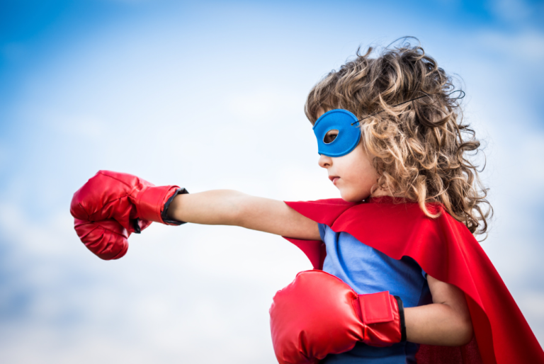 Photo d'une petite fille avec un masque et une cape de super-héros et des gants de boxe rouge pour illustrer le fait que la pratique psychocorporelle et émotionnelle Fight thérapie peut se faire avec des enfants et des adolescents