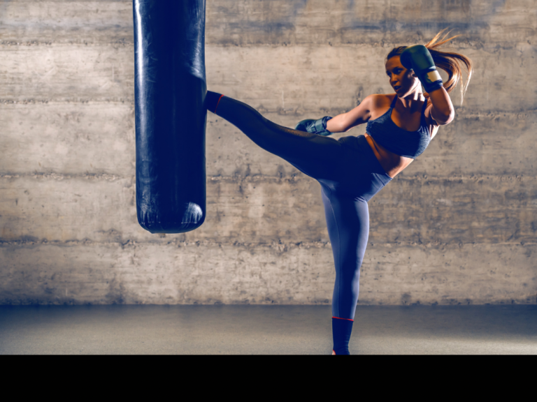 Femme qui met un coup de pied rotatif dans un sac de frappe pour imager la pratique thérapeutique et psychocorporelle de la boxe ou fight thérapie